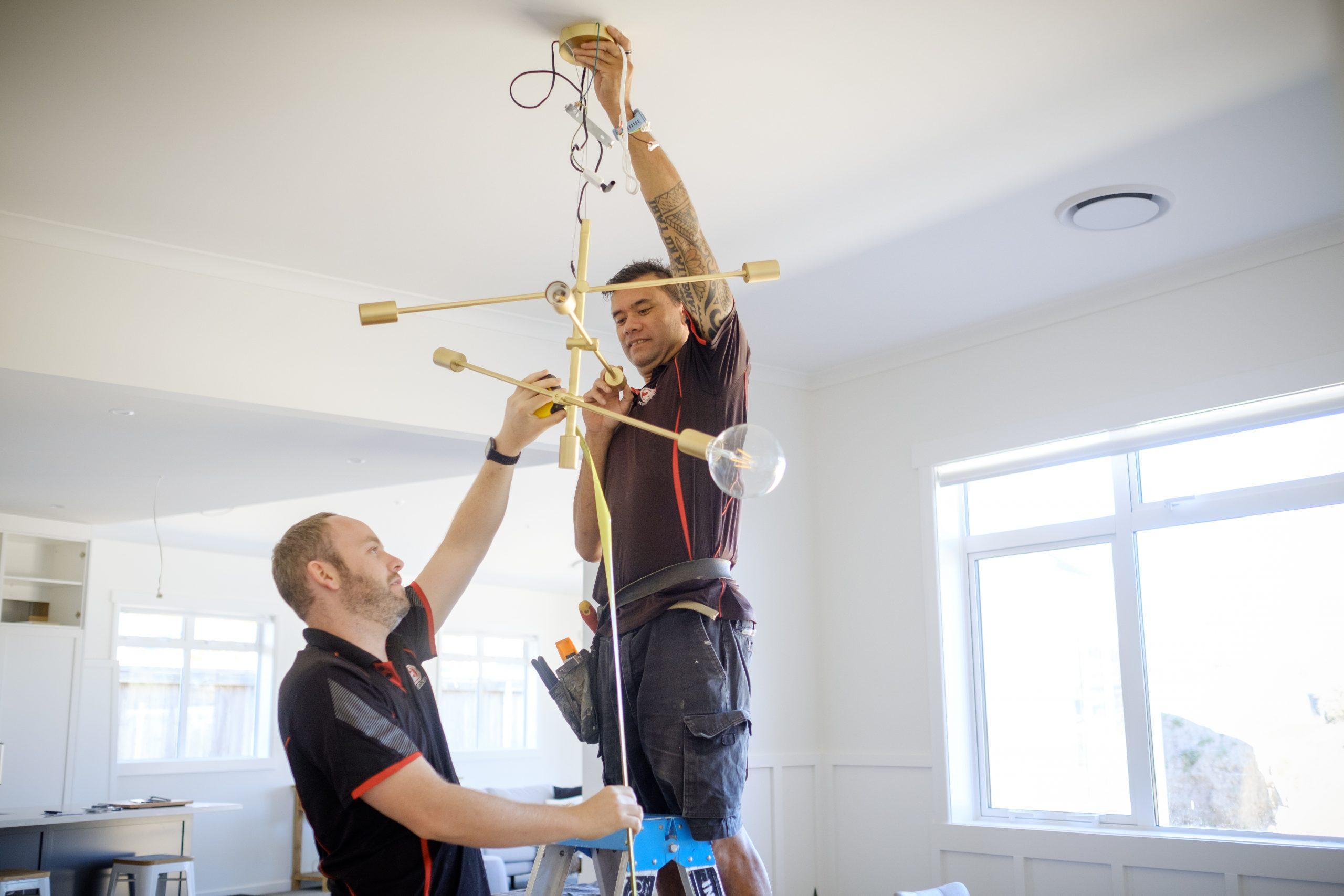 Two 2E Electrical team members installing a modern gold ceiling light in a bright Hamilton residential home